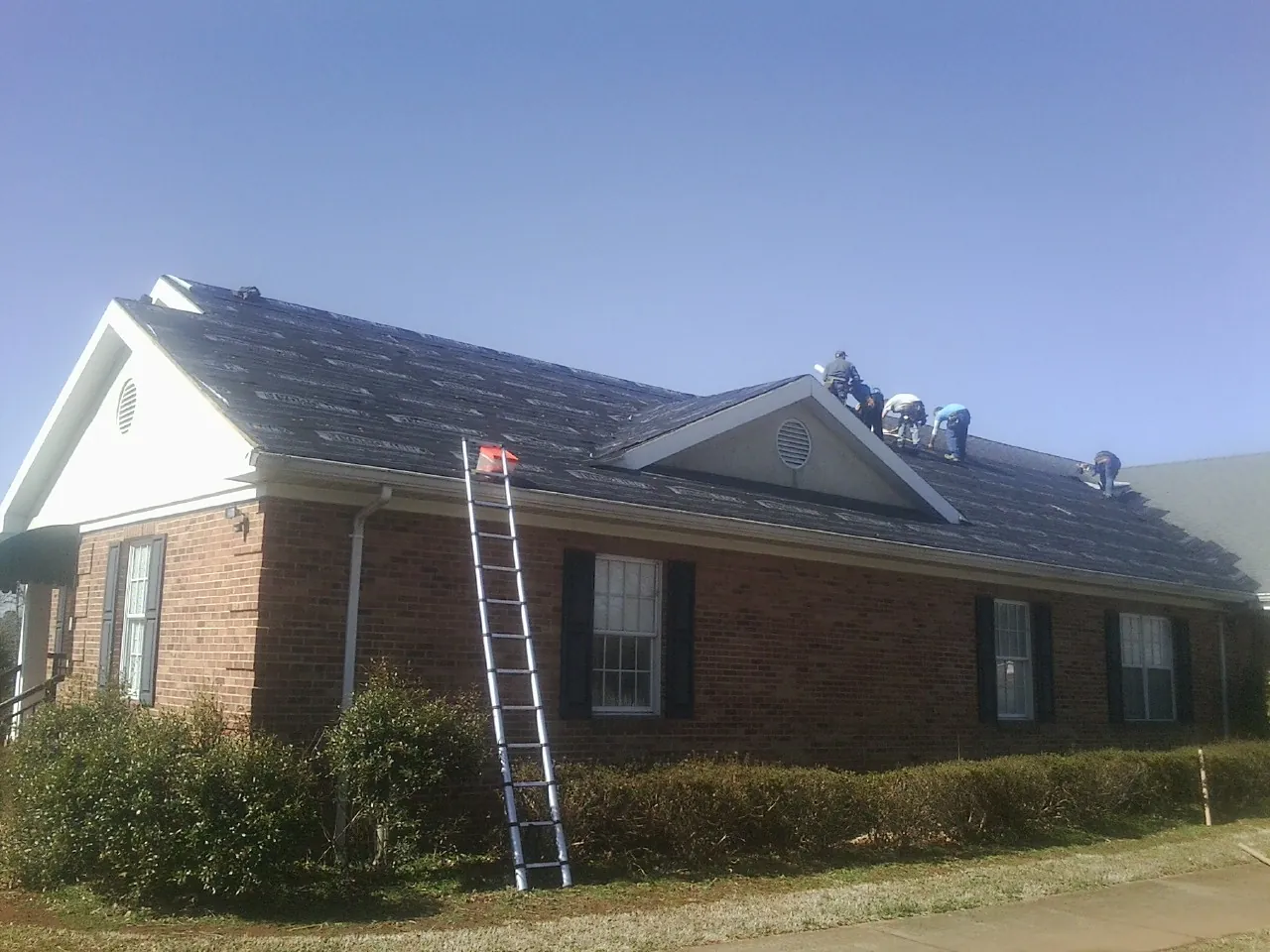 Crew tearing shingles off a brick ranch roof with a ladder set — Metal Roof Repair work by our crew in Trafalgar