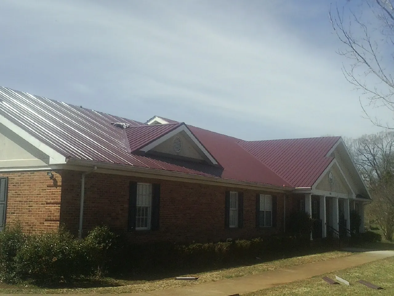 Red metal roof with gabled entries on a long brick building, from a Hail Damage Roof Repair job in Trafalgar