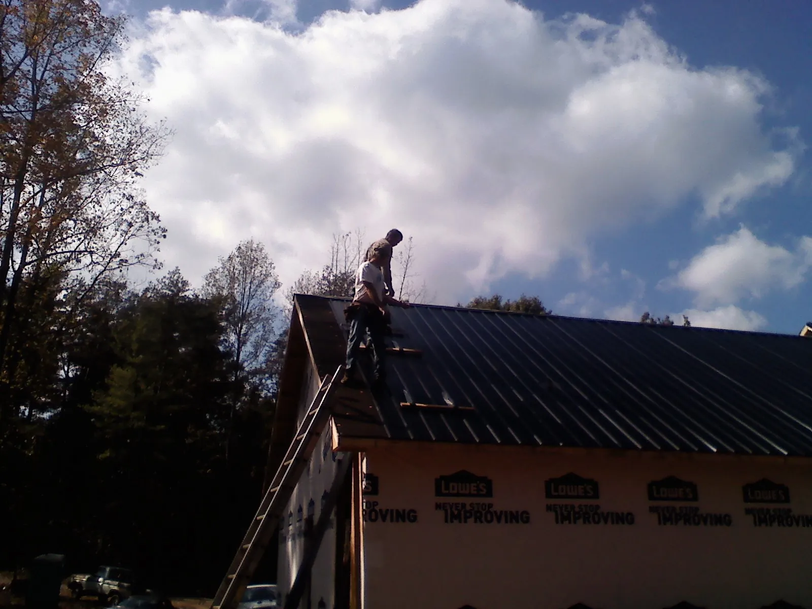 Roofer fastening dark metal panels high against a cloudy sky, from a Roof Inspection job in Trafalgar