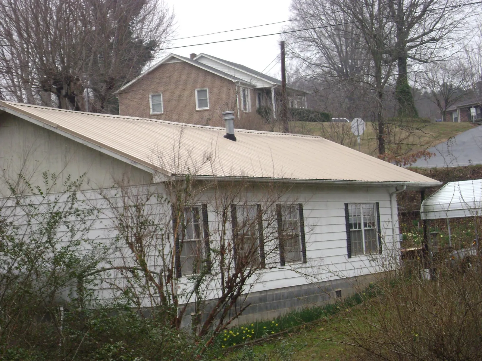 Tan metal roof on a white sided house set into a hillside — Commercial Roofing by Roofing Brothers in Trafalgar